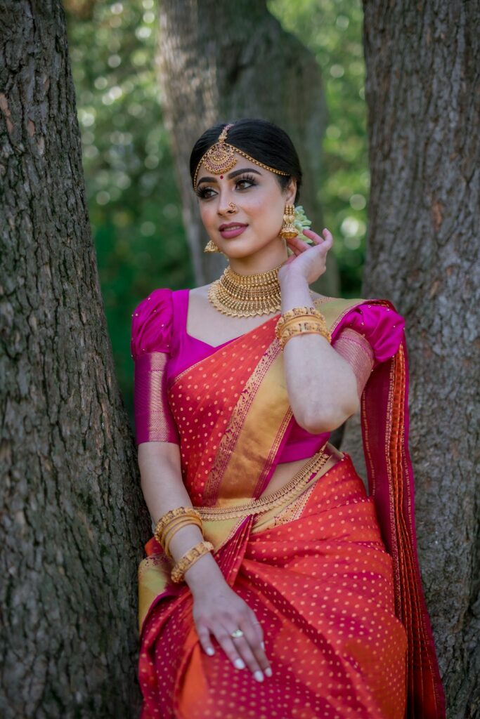 A woman in a pink and orange sari with gold jewellery between two trees